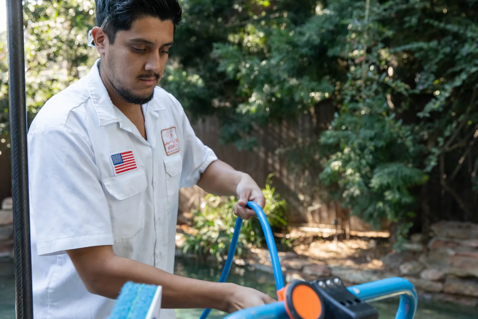 Pool maintenance technician holding a service tool in a residential backyard, pool companies near me