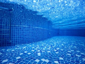 Underwater view of an empty swimming pool in Long Beach CA, with blue patterned tiles covering the floor and walls, and reflections shimmering on the water’s surface.